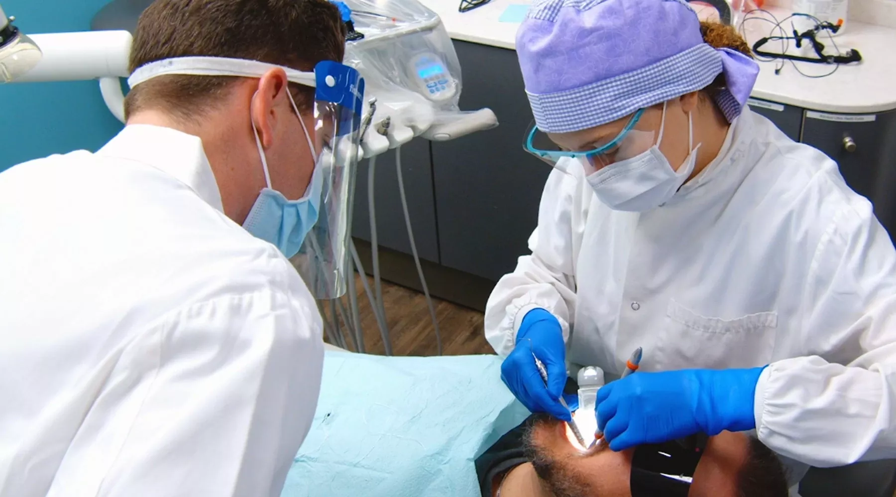 Dentist in white coat working on patient while another dentist looks on