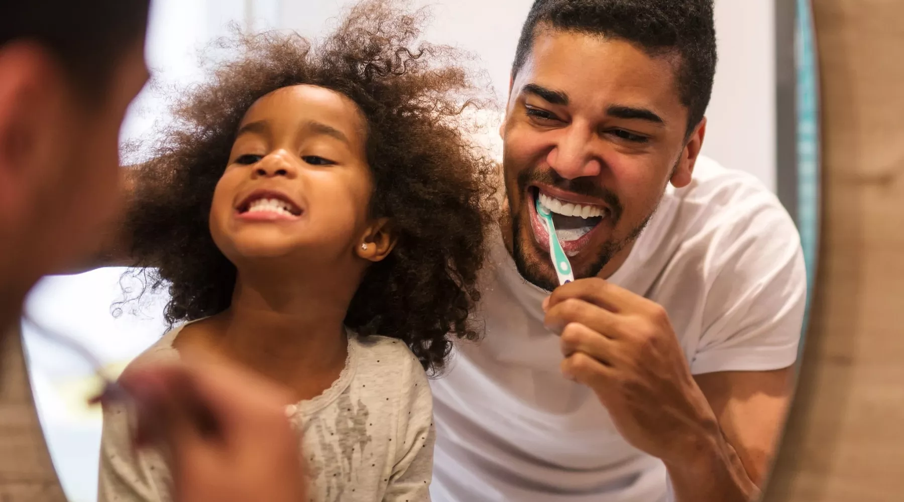 Child and adult brushing teeth looking in a mirror